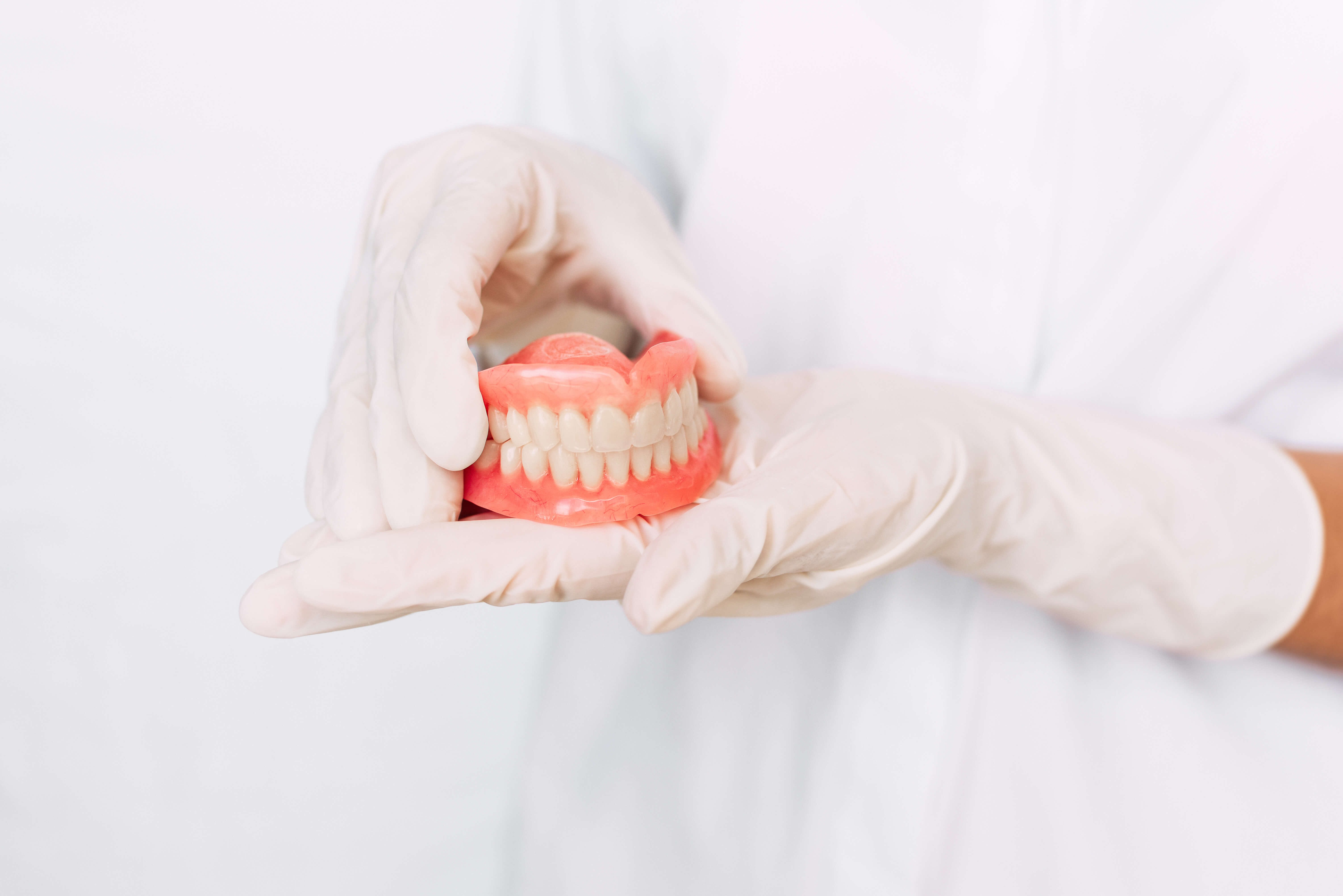 Dental prosthesis in the hands of the doctor close-up. Dentist holding ceramic dental bridge. Front view of complete denture. Dentistry conceptual photo. Prosthetic dentistry. False teeth Dental prosthesis in the hands of the doctor close-up. Dentist holding ceramic dental bridge. Front view of complete denture. Dentistry conceptual photo. Prosthetic dentistry. False teeth